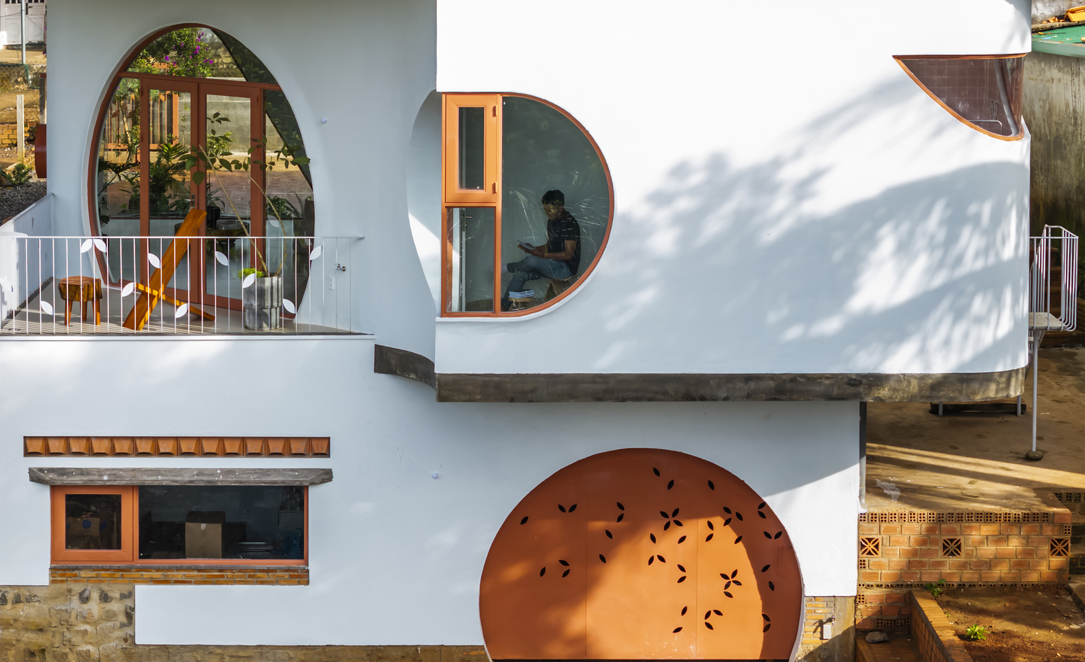 White facade with circular and arched timber-framed openings casting tree shadows in afternoon light