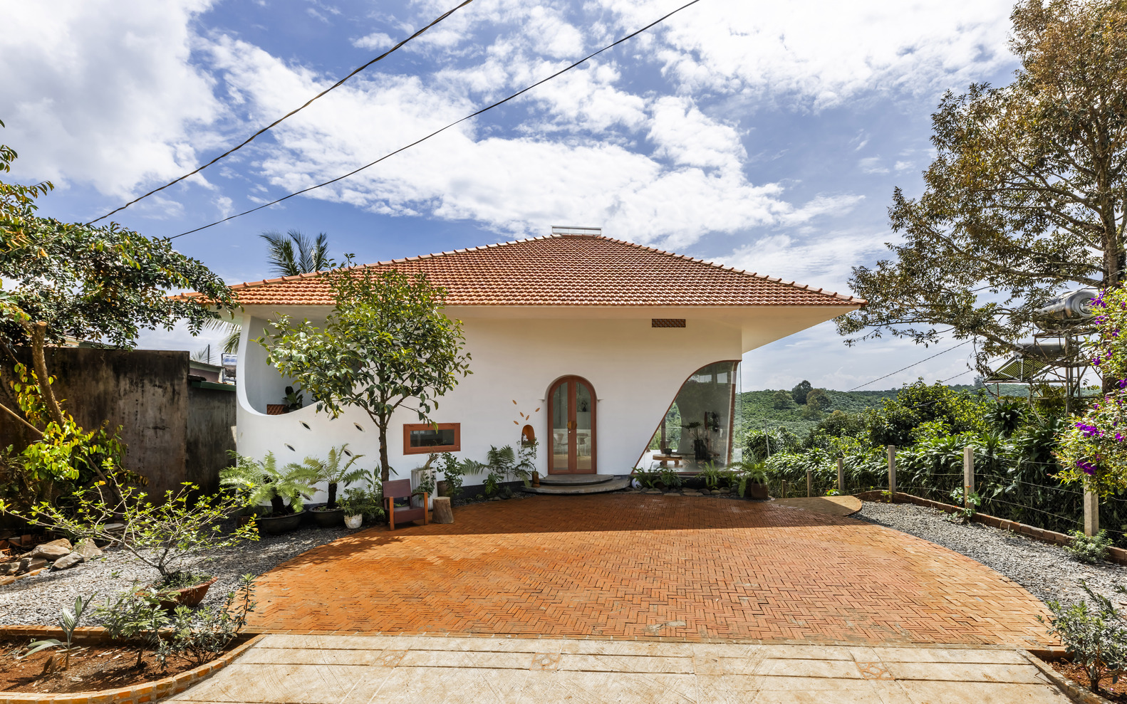 Red clay tile roof over white walls with herringbone brick courtyard and surrounding foliage
