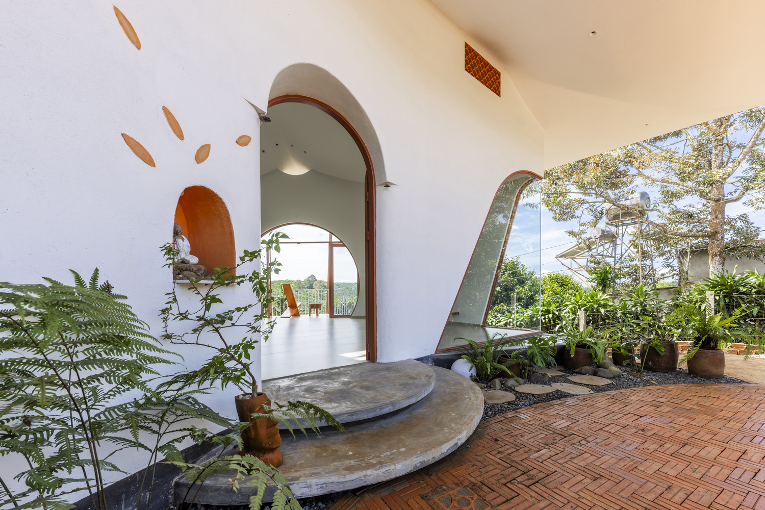 Concrete steps leading through arched entry with wall cutouts and potted plants on brick paving