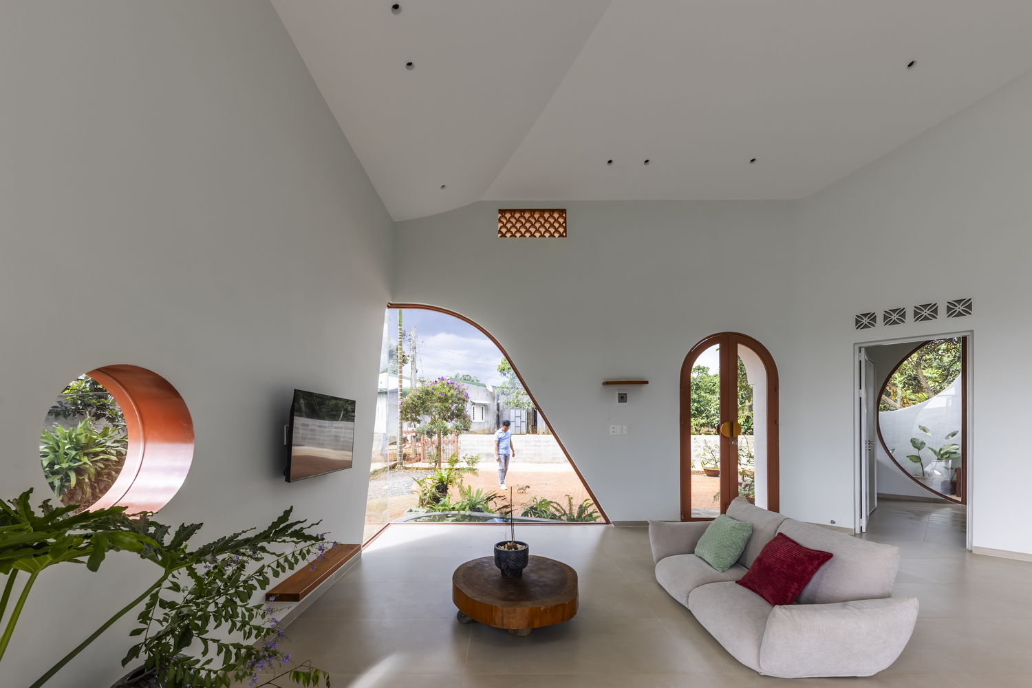 Living room with vaulted ceiling and asymmetric glazed opening framing a courtyard with person walking