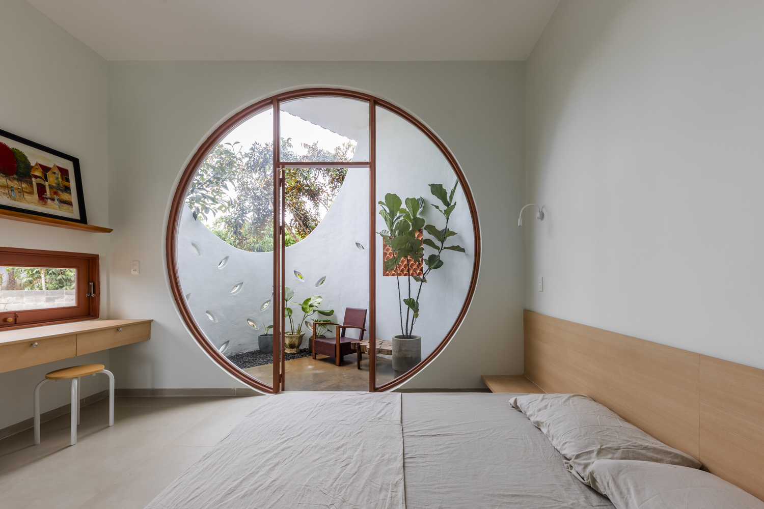 Bedroom with circular timber-framed door opening to a private courtyard with armchair and plants