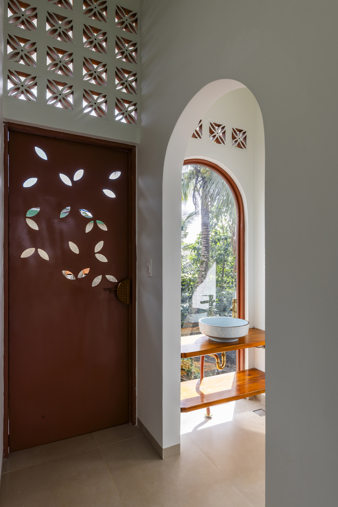 Arched bathroom niche with timber vanity and perforated door with leaf-shaped cutouts