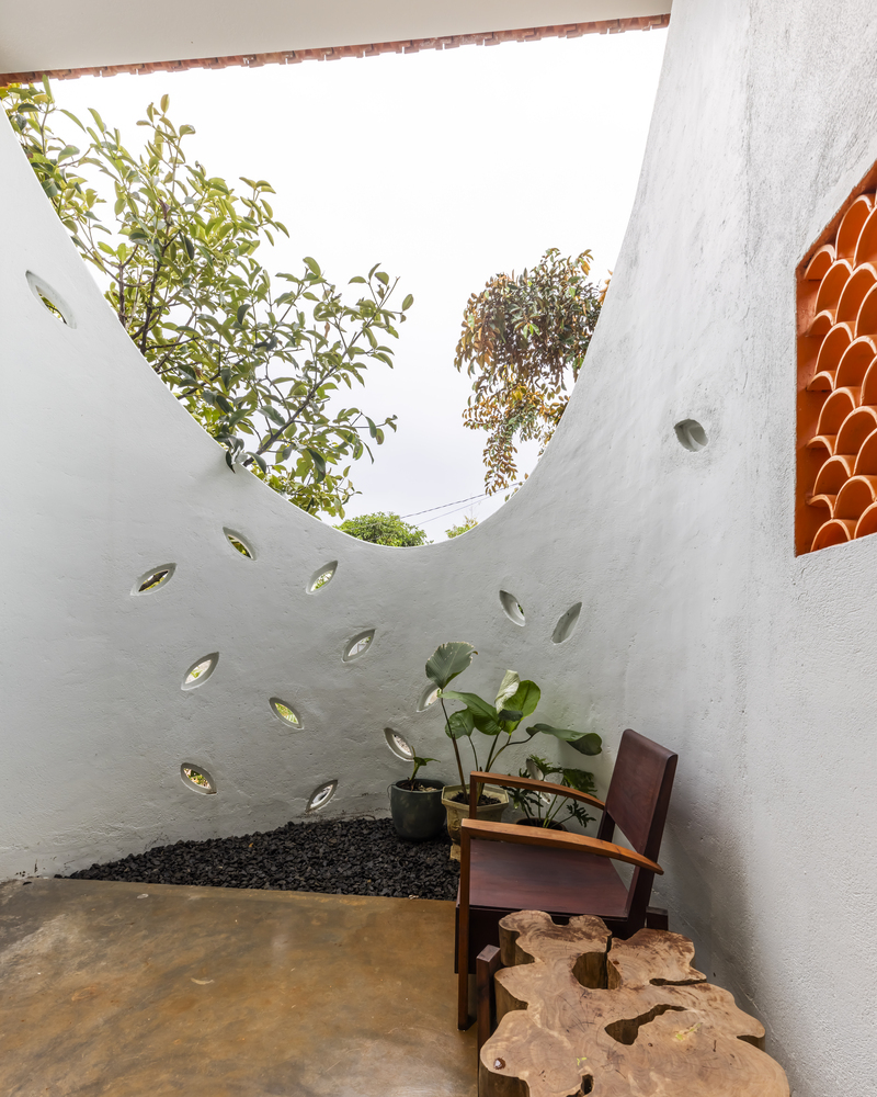 Planted courtyard with curved white wall punctured by leaf-shaped openings and open sky above