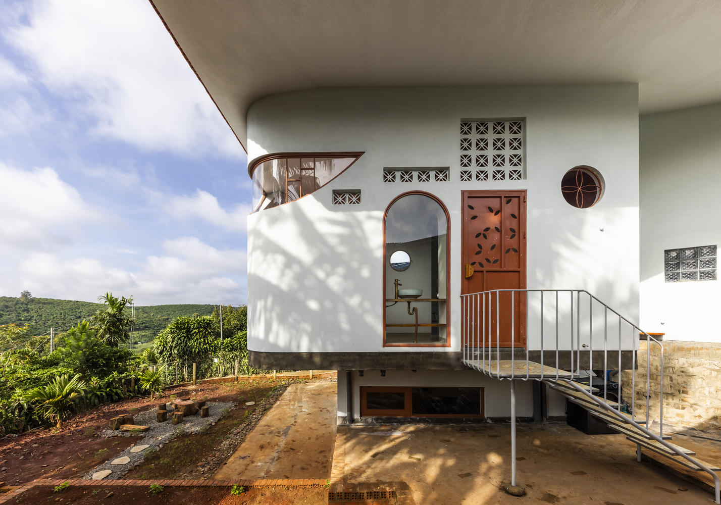 Elevated white facade with circular and arched openings connected by metal staircase in afternoon sun