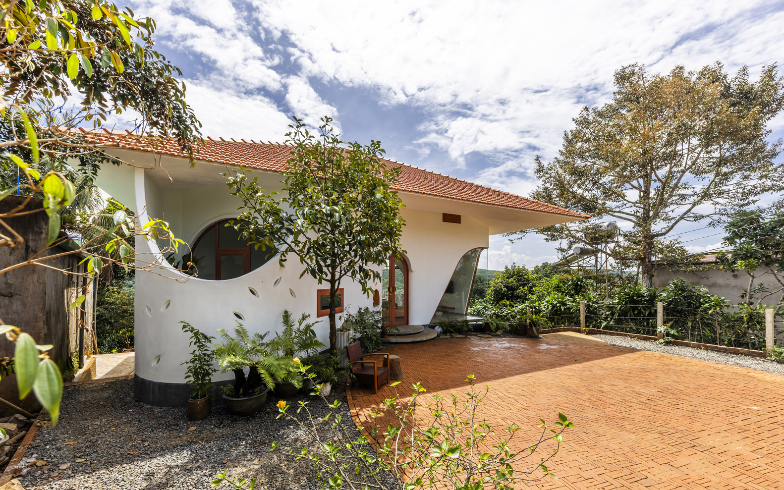 White stucco house with circular and arched openings on a terracotta-paved terrace surrounded by potted plants