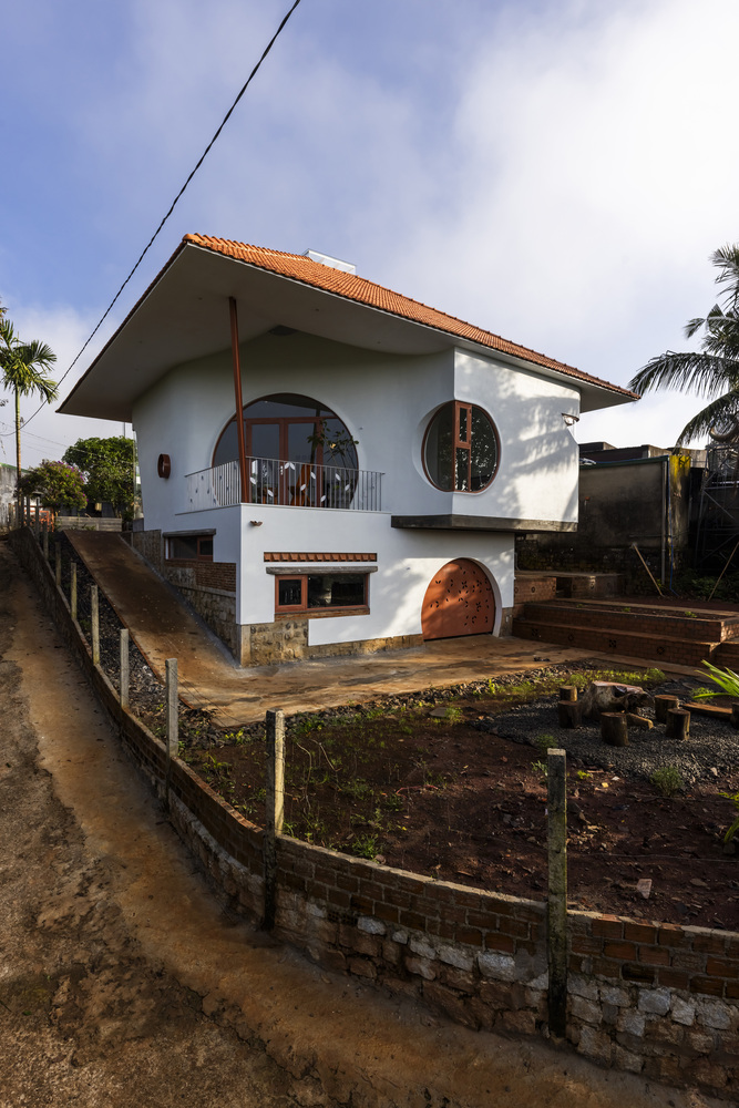 White facade with circular and arched openings above a brick retaining wall with terraced garden beds