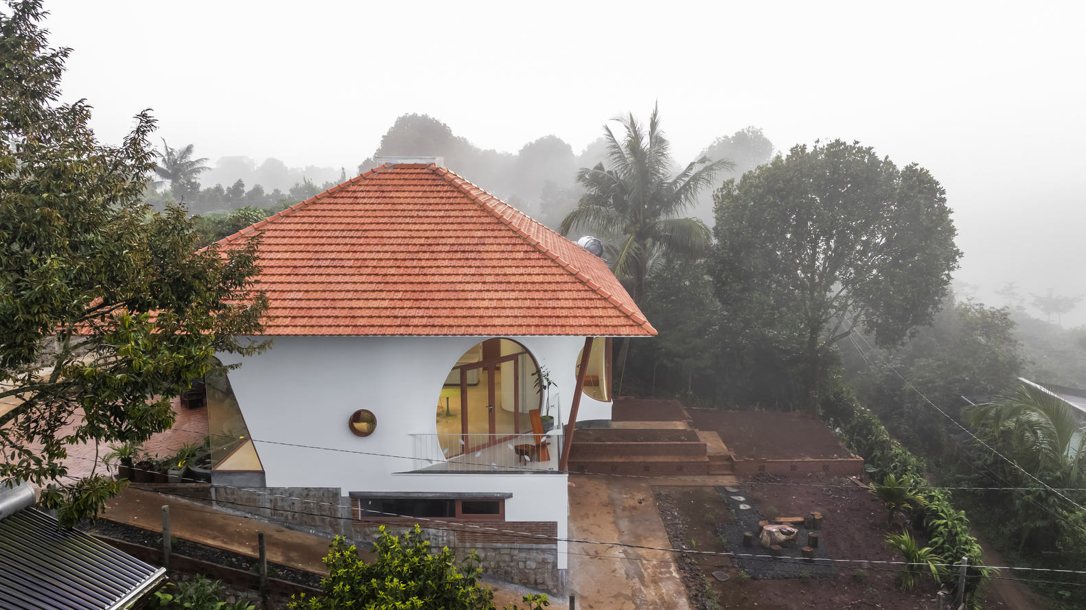 Elevated view of the terracotta-tiled pyramidal roof and arched terrace openings in heavy morning fog