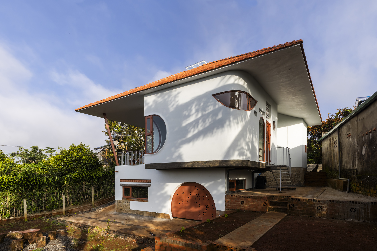 Side elevation showing the overhanging terracotta roof and circular windows casting shadows on white stucco walls
