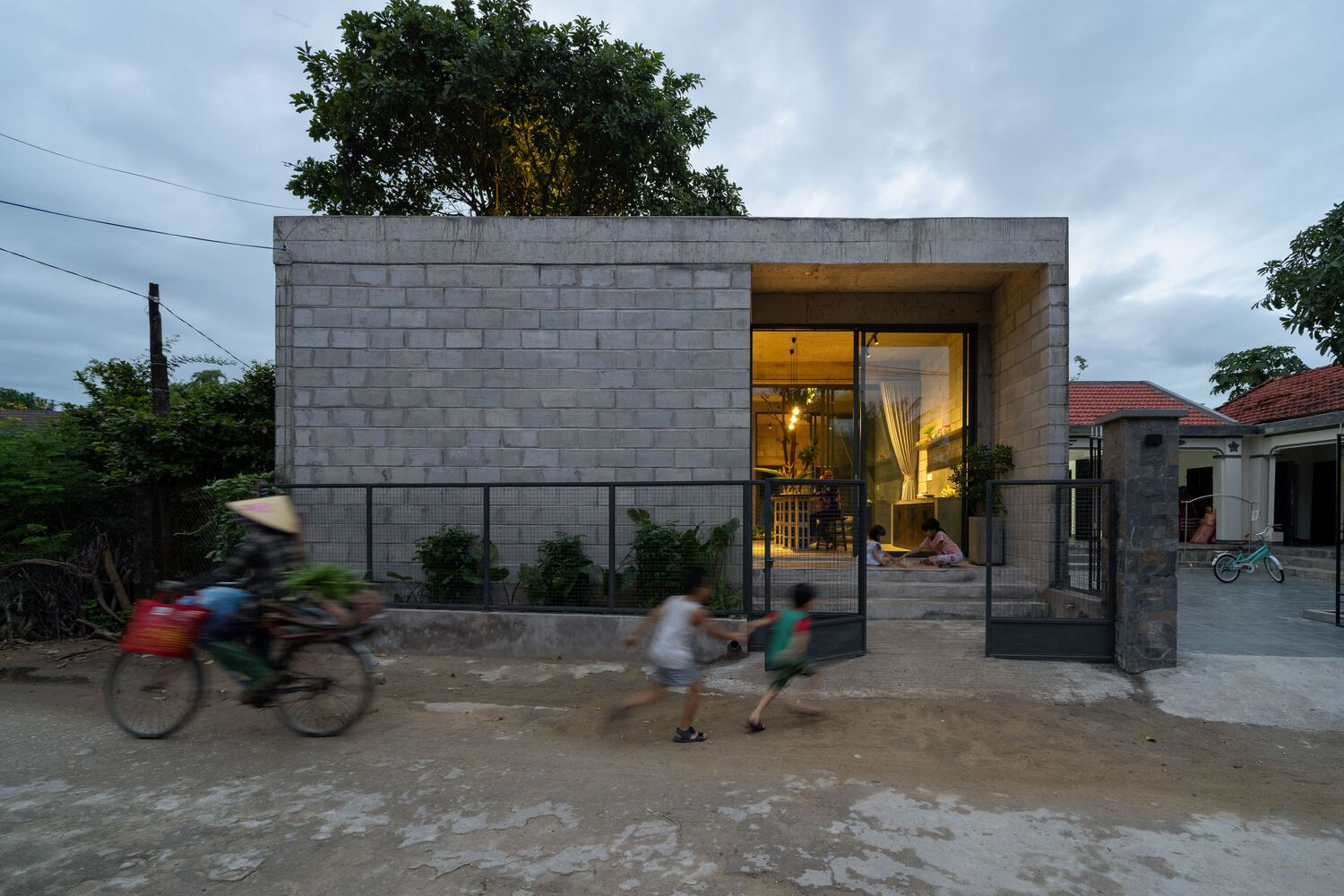 Street view of the concrete block facade with recessed entrance as motorbikes and pedestrians pass