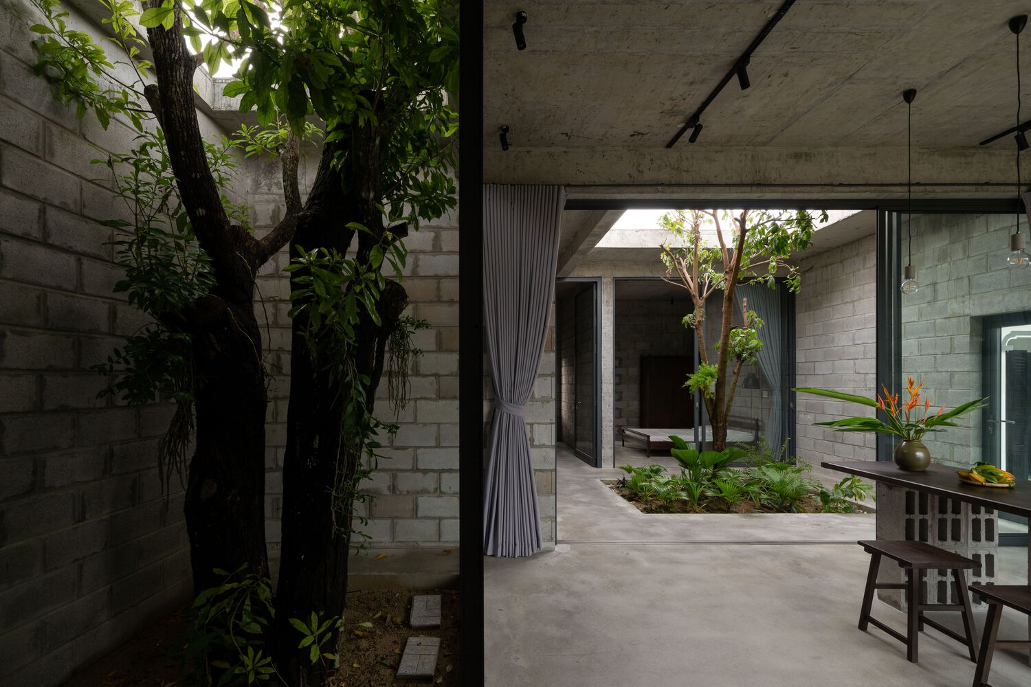 Interior corridor with exposed concrete ceiling and curtained opening framing the central courtyard with trees