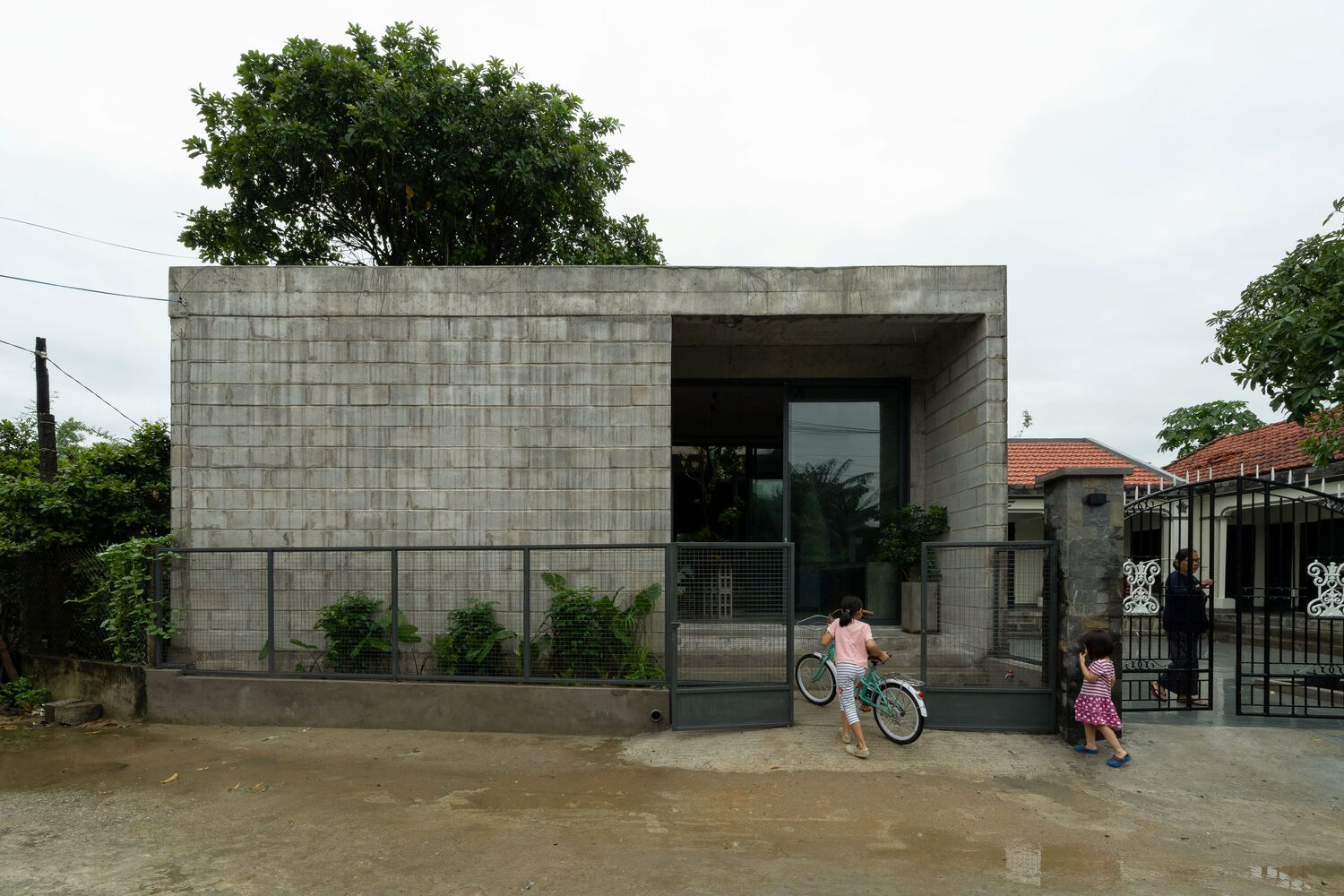 Front facade in grey concrete block with children on bicycles in the street foreground