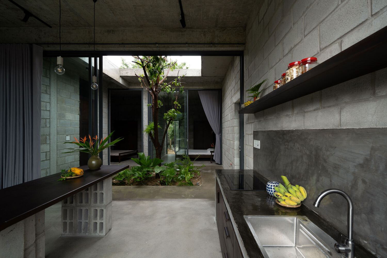 Kitchen with concrete walls and polished black countertop overlooking an interior planted courtyard through glazed openings