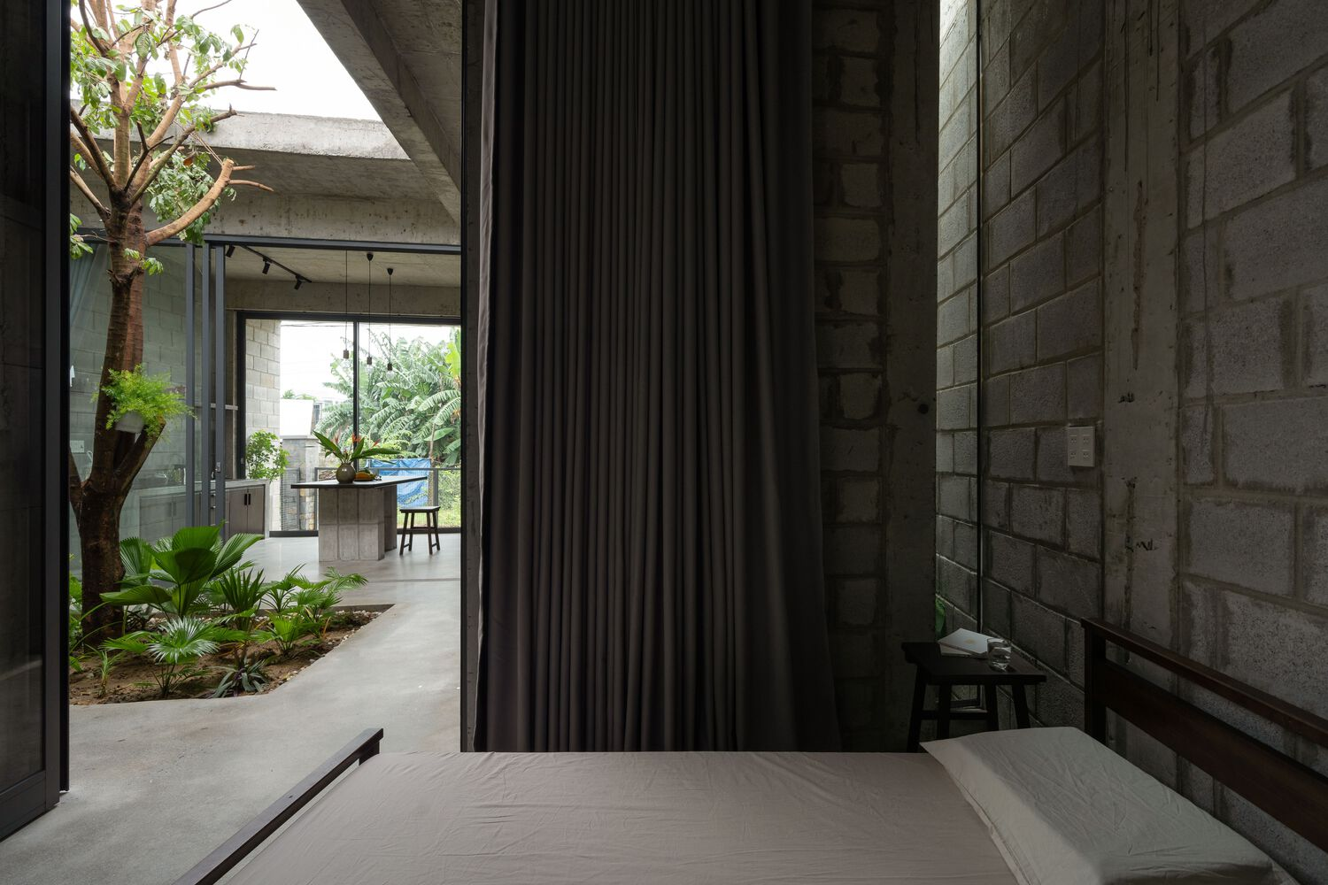Bedroom with timber platform bed and grey curtains opening to the planted courtyard