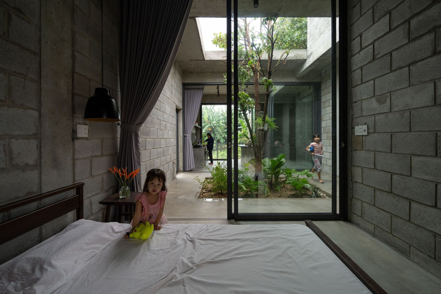 Bedroom with concrete block walls opening to an interior courtyard planted with trees and greenery