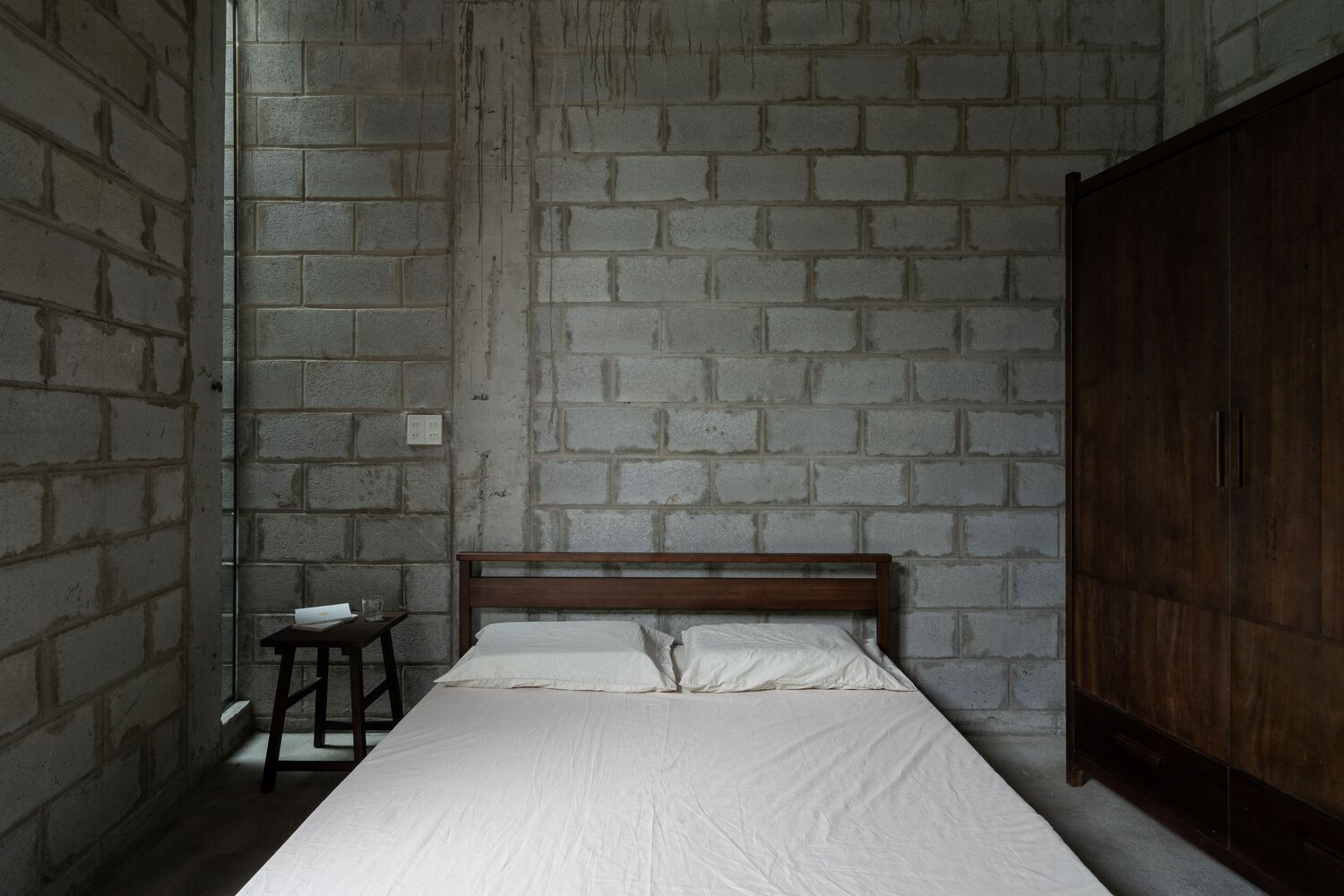 Bedroom corner showing exposed concrete block walls and concrete beam ceiling in natural light