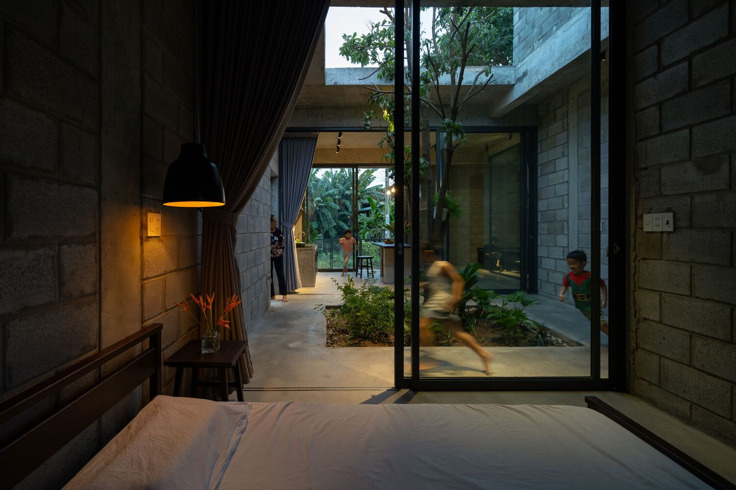 Bedroom view through glazed doors to interior courtyard with children moving through at dusk