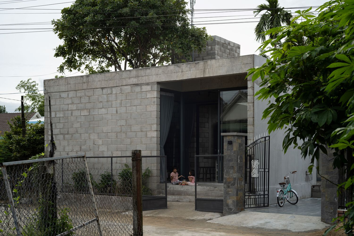 Street view of concrete block facade with open entrance framed by chain-link fence and parked bicycle