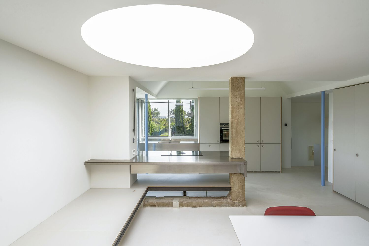 Kitchen with circular ceiling skylight and cantilevered counter wrapping the exposed concrete column