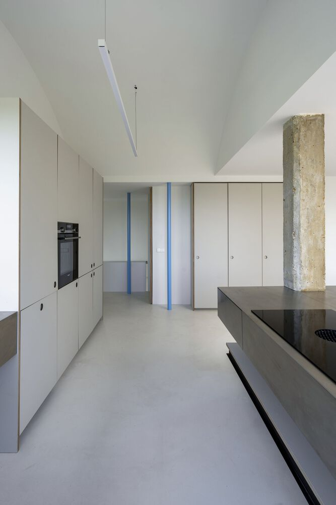 Kitchen corridor with pale cabinetry, blue columns, and linear pendant light under vaulted ceiling