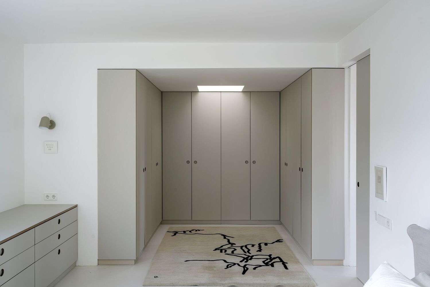 Bedroom with floor-to-ceiling storage cabinets and rug featuring calligraphic motif under skylight