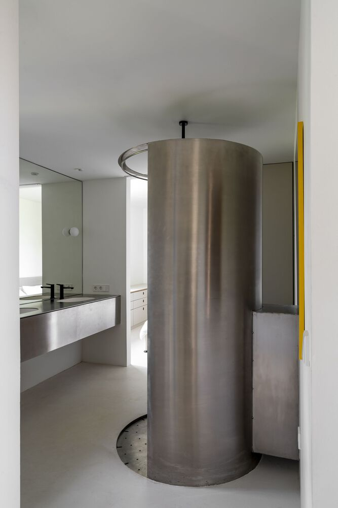 Cylindrical stainless steel shower enclosure with ceiling-mounted circular ring and perforated base in a white bathroom