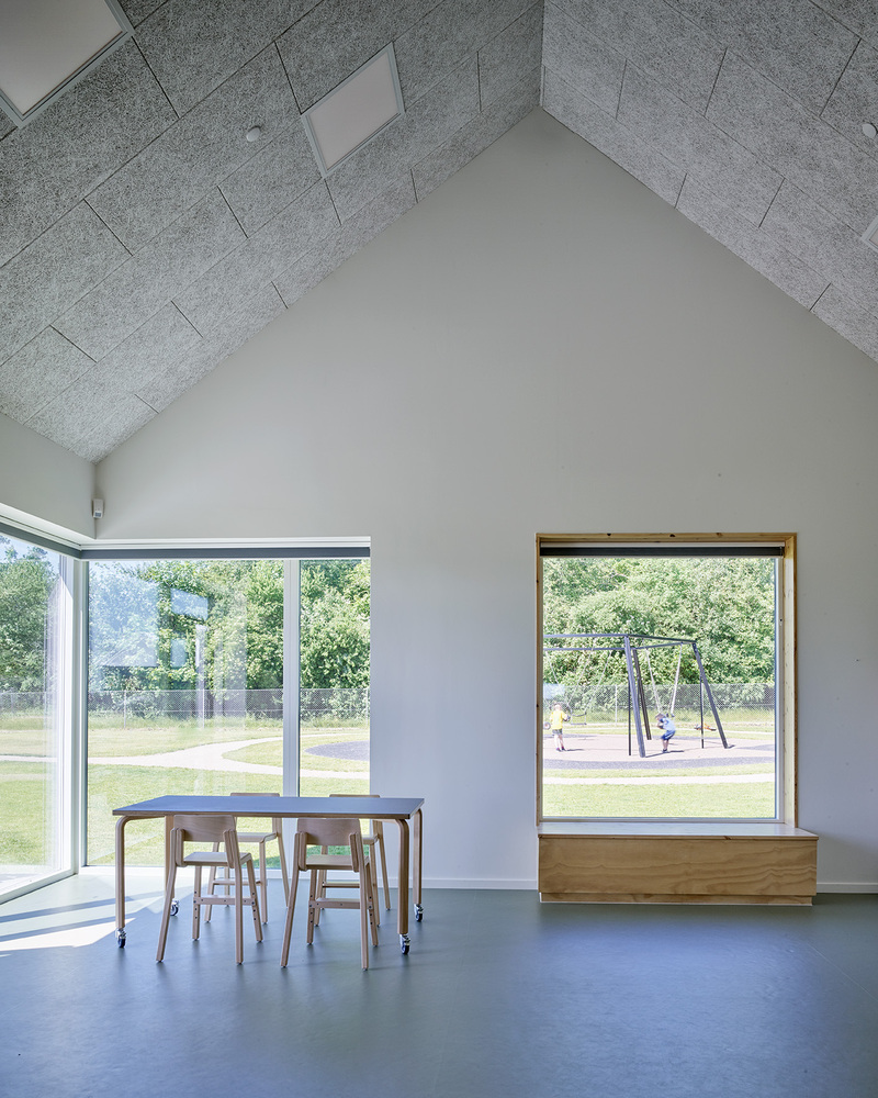 Interior classroom space with herringbone acoustic ceiling panels and views to a playground through framed windows