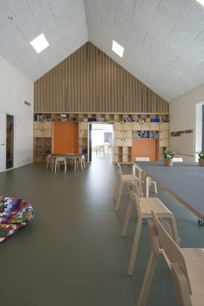 Interior classroom with vertical timber accent wall, plywood storage units, and roof skylights above grey flooring