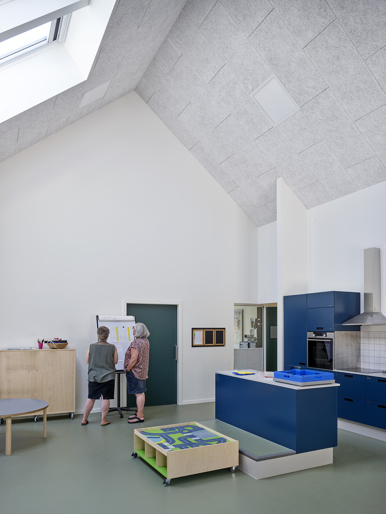Open-plan interior with blue kitchen island, acoustic ceiling tiles and two children working at a wall-mounted desk