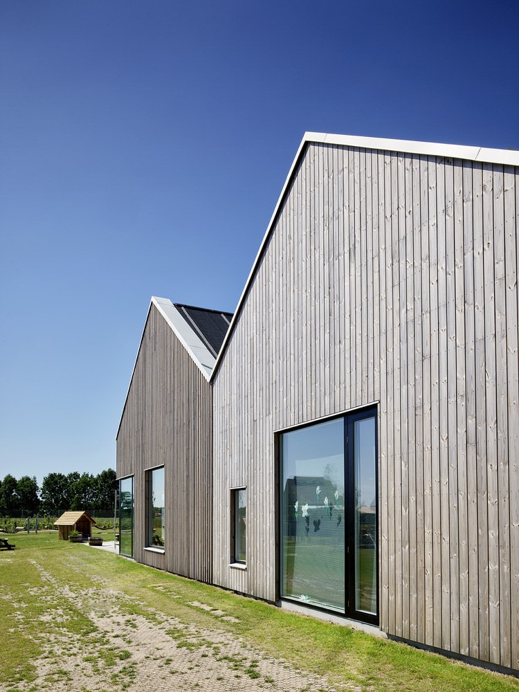 Vertical timber cladding with narrow windows on gabled end wall under clear blue sky