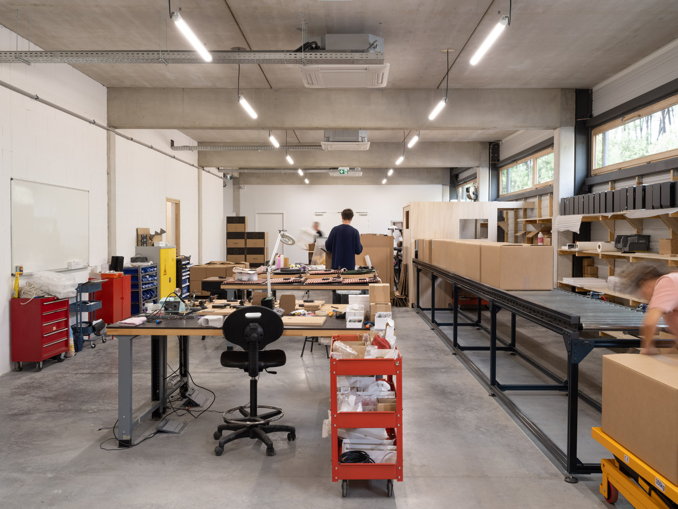 Workshop space with people moving past workbenches loaded with materials and cardboard samples