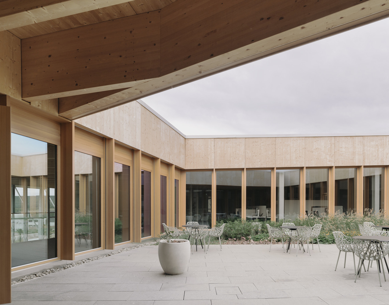 Interior courtyard with timber-framed glazing, planted beds, and outdoor seating under timber ceiling