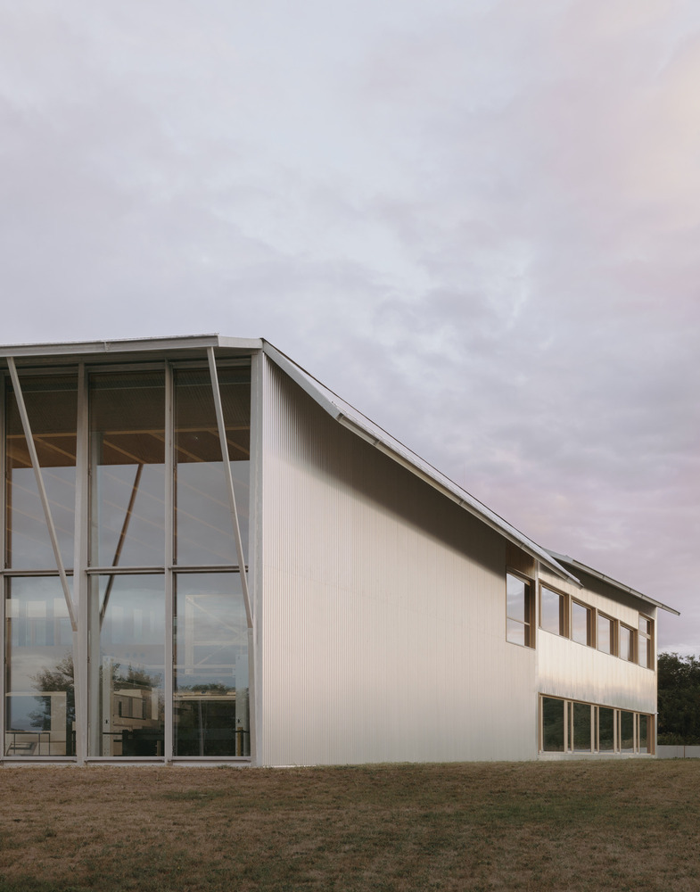 Corner facade with glass-walled entrance, diagonal bracing, and corrugated metal cladding under overcast sky
