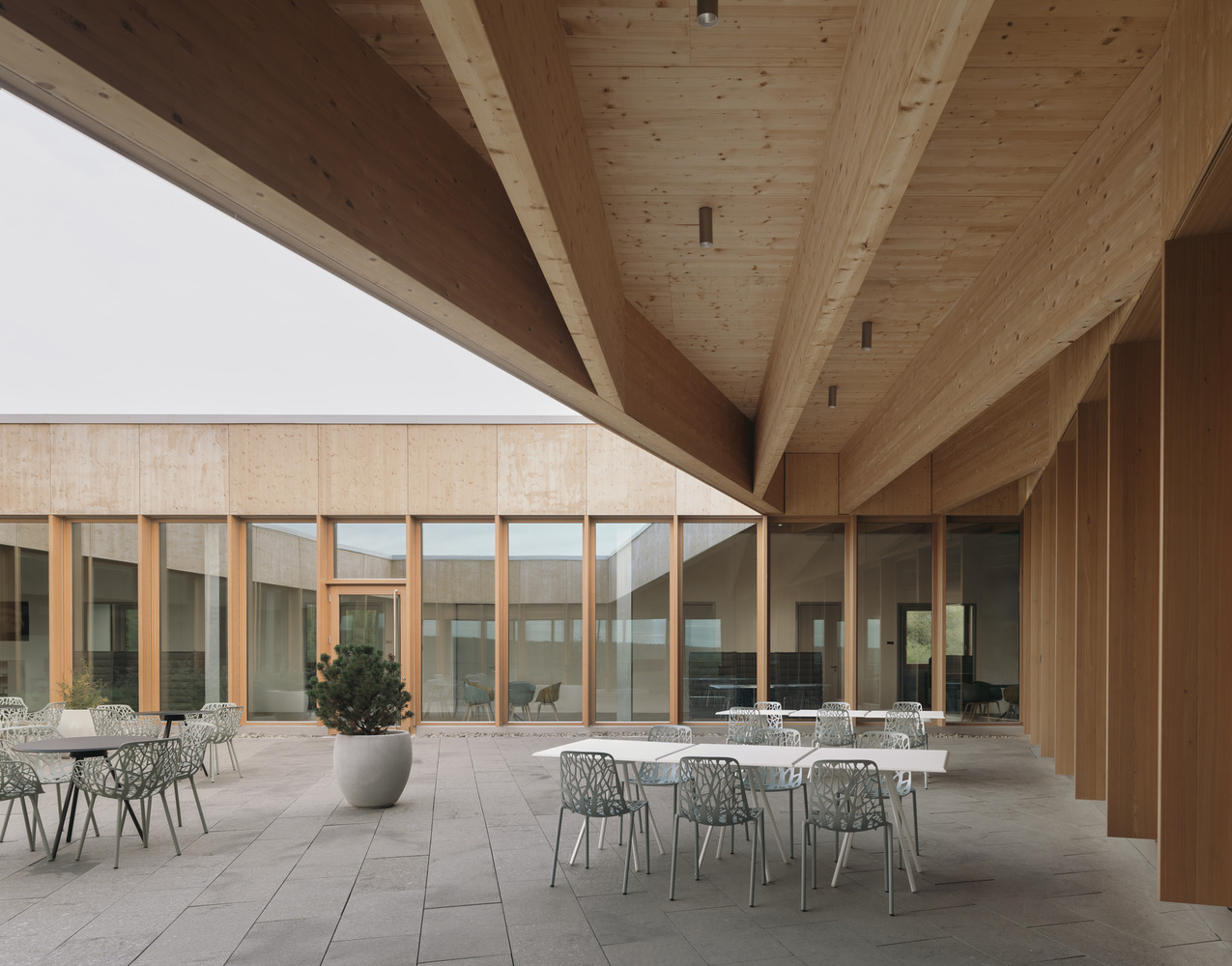 Covered courtyard with exposed timber beams, tiled floor, dining tables, and potted tree