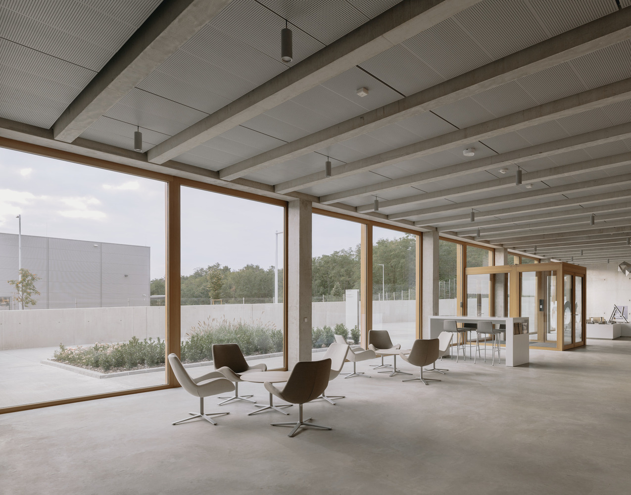 Interior lobby with timber beams, full-height glazing, lounge chairs, and view to planted courtyard