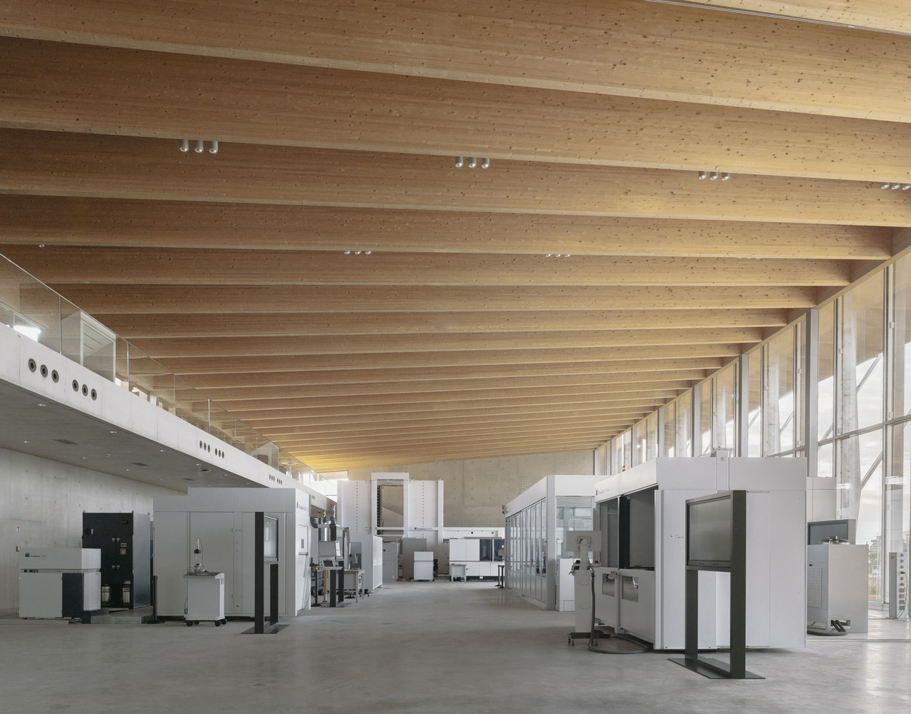 Exhibition hall with exposed timber ceiling beams, track lighting, and display cases on concrete floor