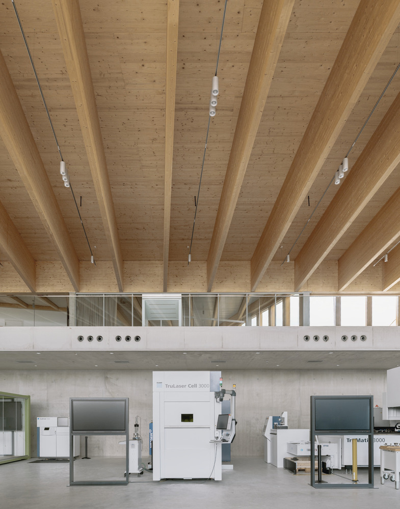 Double-height space with laminated timber beams, mezzanine walkway, and industrial equipment on ground floor
