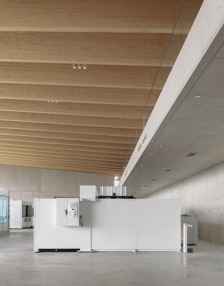 Double-height interior space with exposed timber beam ceiling and white equipment modules on polished concrete floor