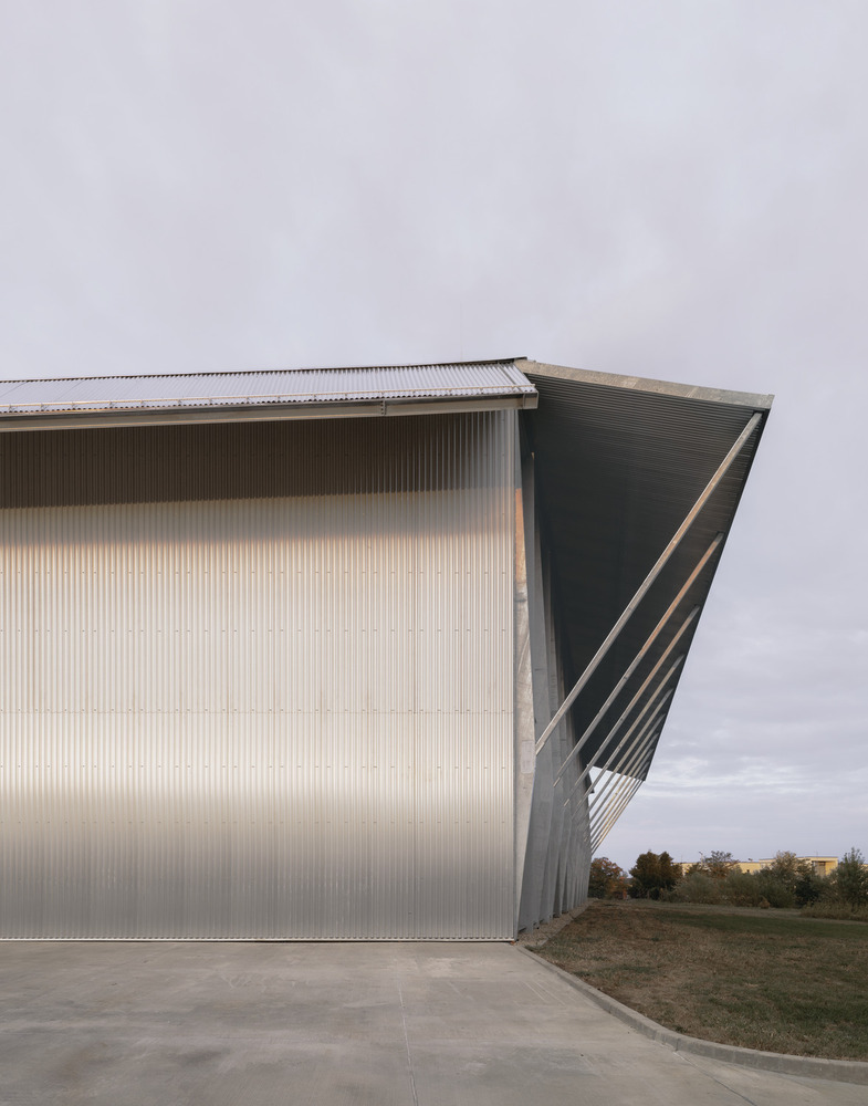 Exterior corner detail of corrugated metal cladding with folded roof edge under cloudy sky