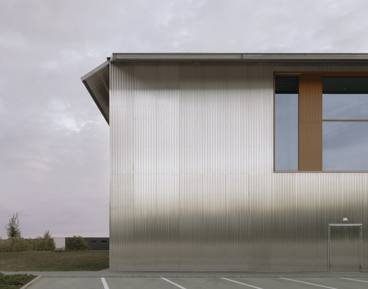 Angled facade of ribbed metal cladding with timber-framed window opening at dusk