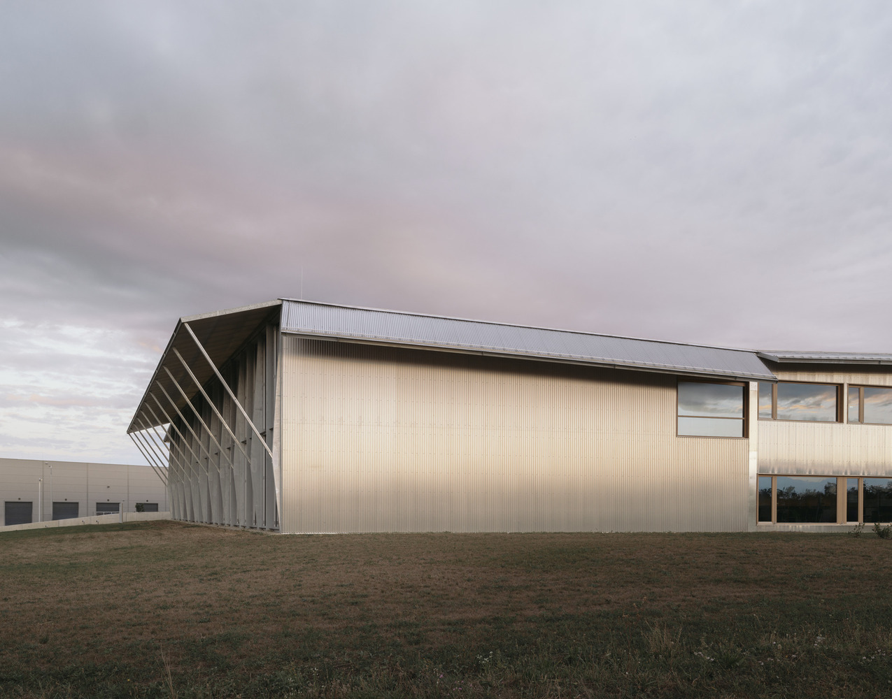 Side elevation showing the corrugated metal cladding and angled steel colonnade across open grassland