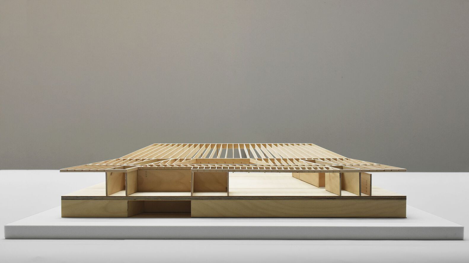 Physical model showing a low pavilion with slatted timber roof and bronze base on a neutral plinth
