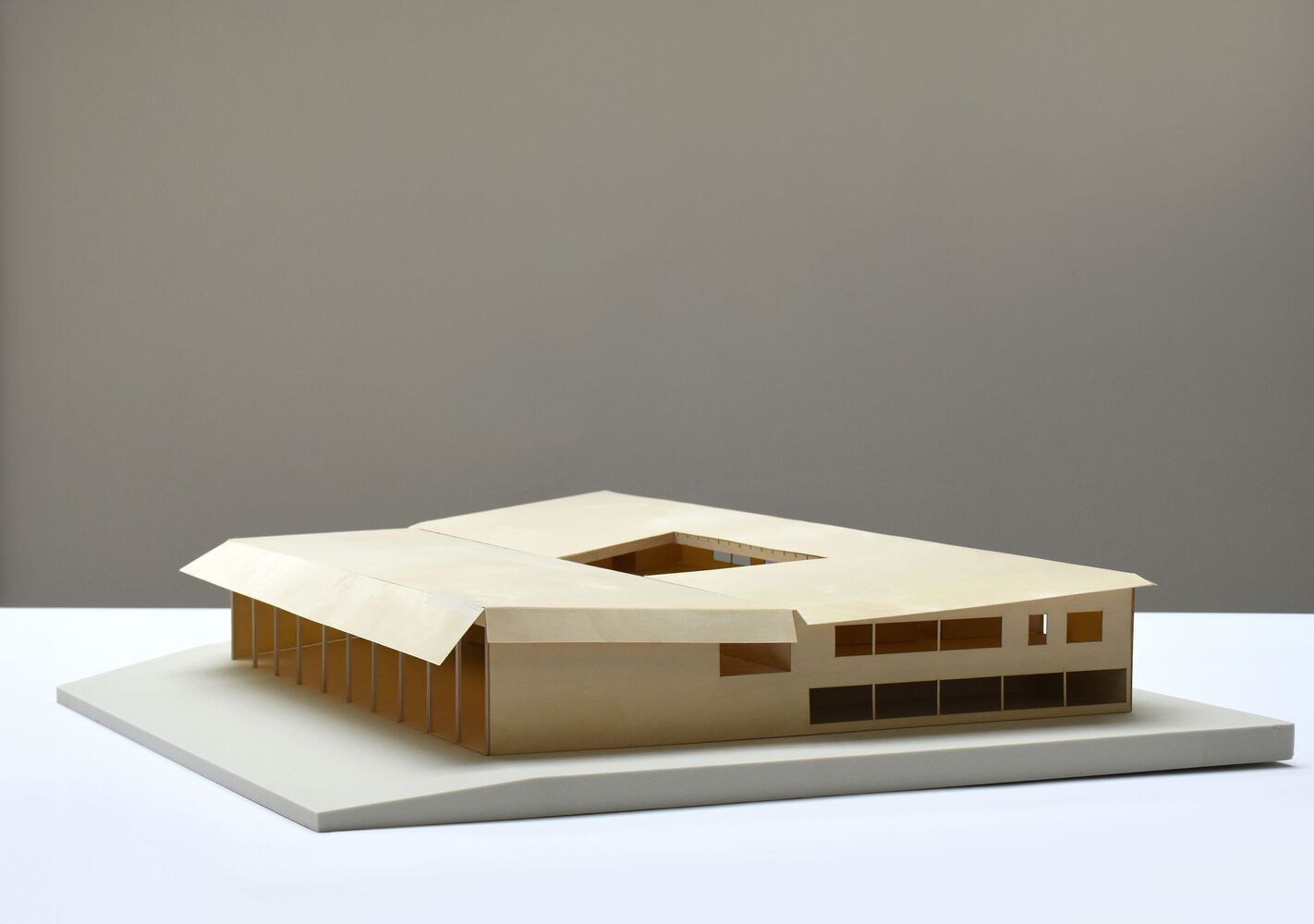 Physical model showing square courtyard void ringed by white roof and bronze colonnade in neutral studio light