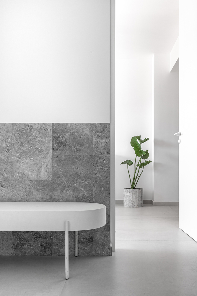 Hallway corner with grey stone wainscoting, white walls, and potted plant beside round table