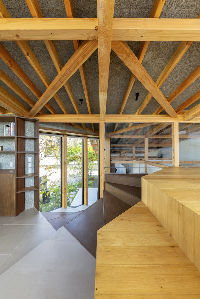 Double-height void: timber rafter ceiling and sloped roof, timber bench seat, glass wall to the garden with a tree visible, plaster walls
