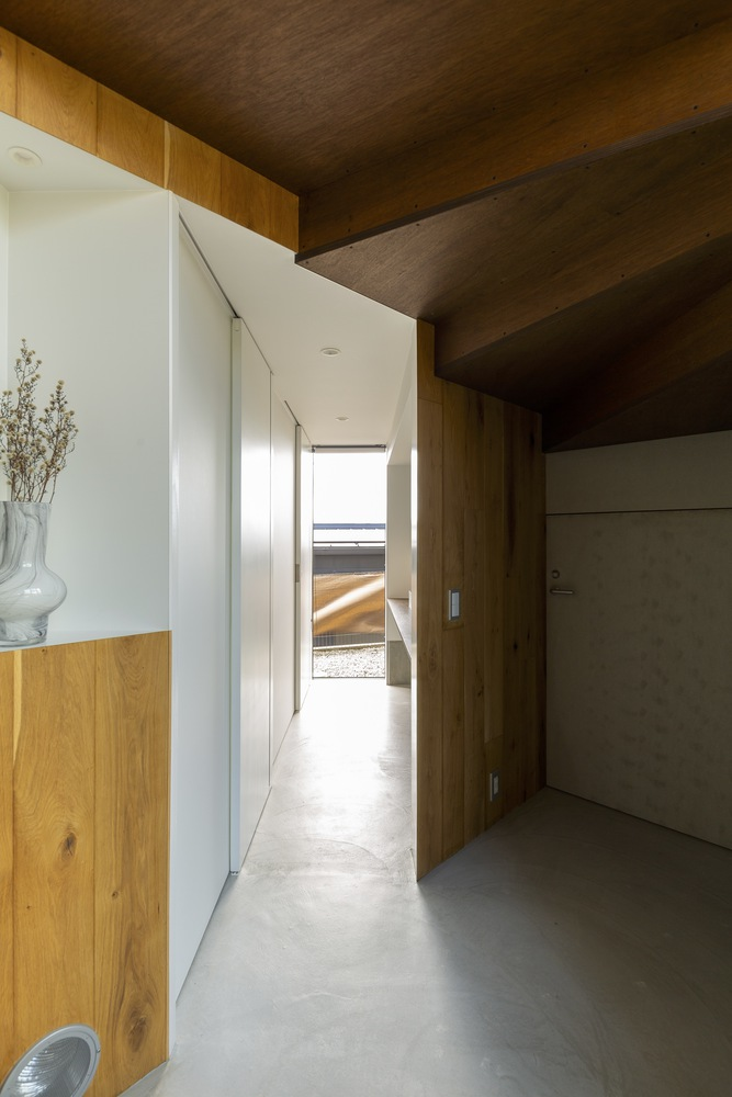 Ground-floor corridor: white sliding door, timber-lined alcove with dried flowers in a ceramic vase, concrete floor, exposed timber structure above