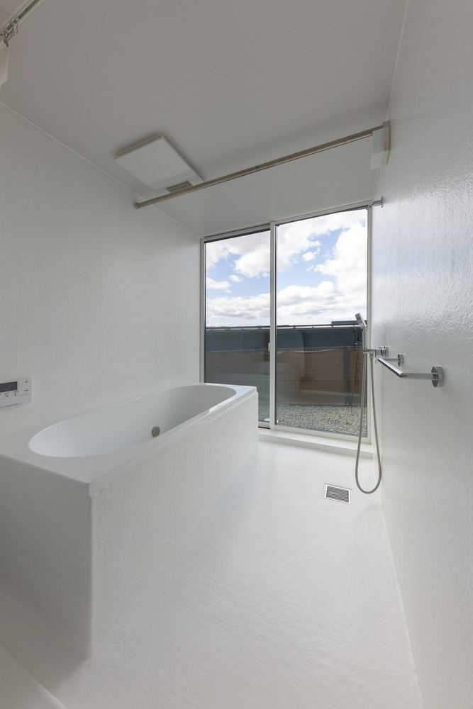 Bathroom: white tile walls, freestanding oval tub, tall window opening to a balcony, wall-mounted shower and grab rail
