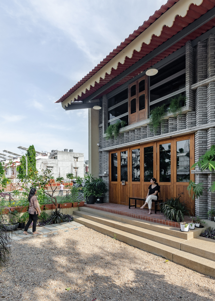 Stepped entrance terrace with timber doors and planters below a tiled roof overhang in daylight