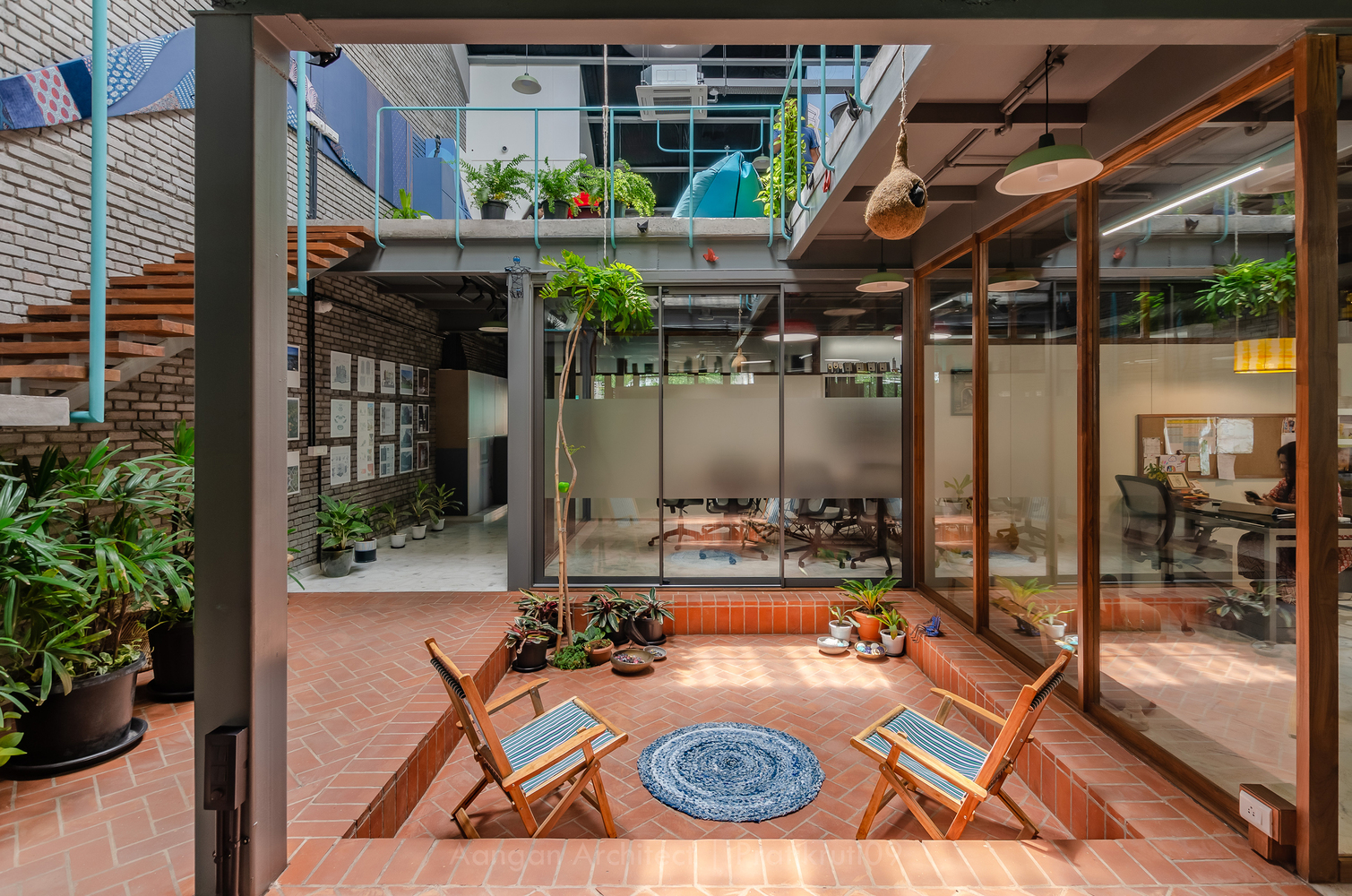 Central courtyard with terracotta floor and folding chairs surrounded by glass walls and upper-level balconies with plants