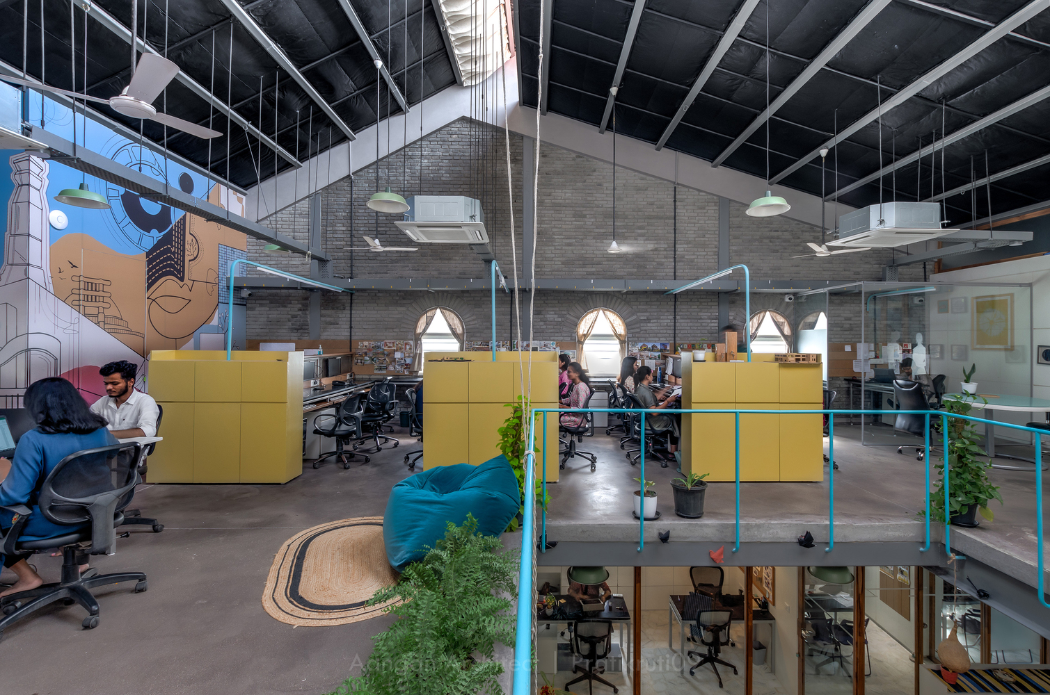 Open-plan workspace with yellow partitions and exposed black ceiling trusses under bright pendant lights