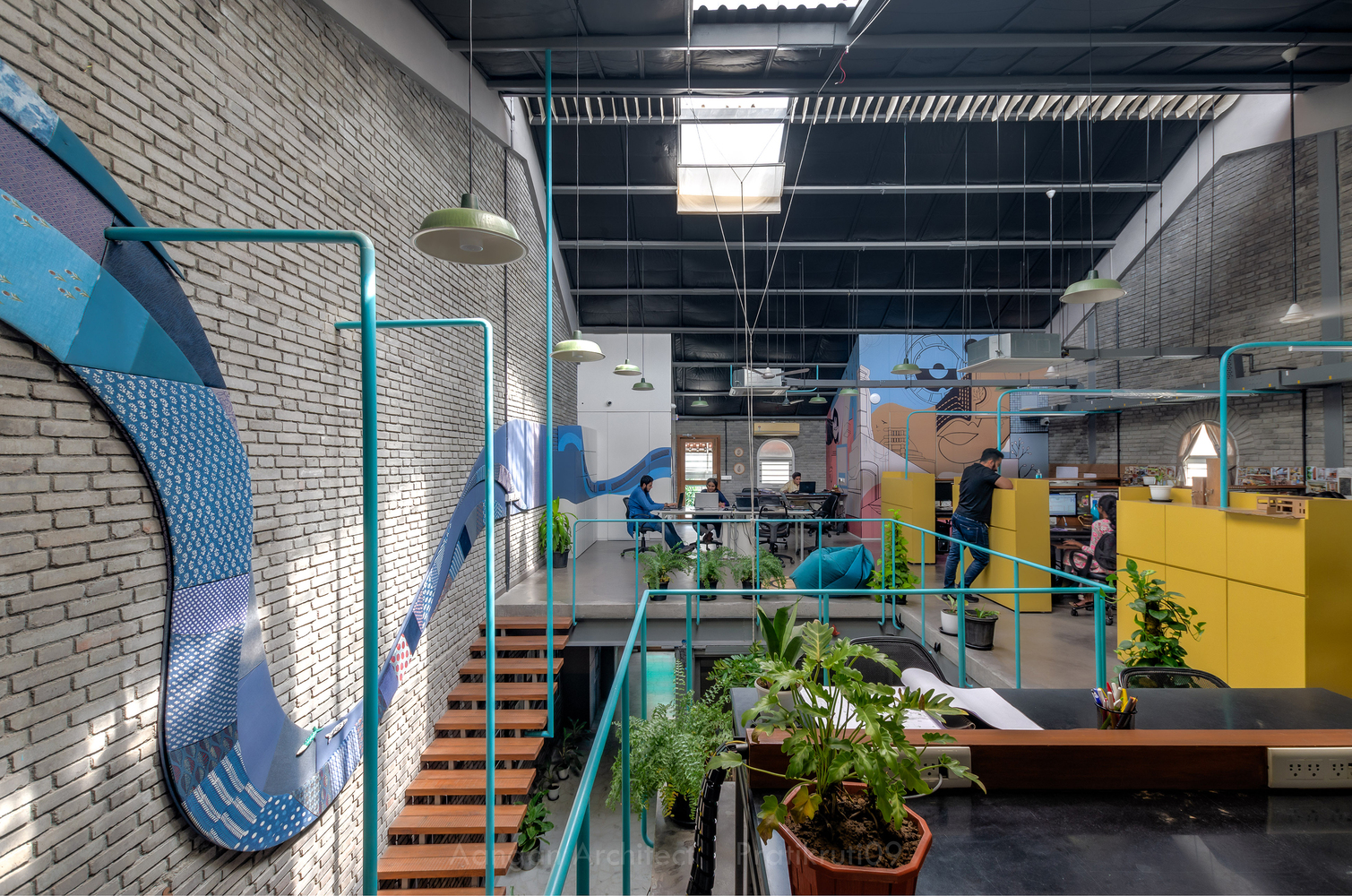 Interior view of double-height office space with painted brick murals and turquoise steel railings around mezzanine